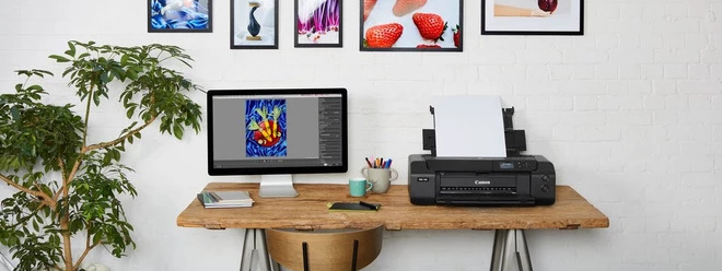 Bureau met een computer en een Canon printer en aan de muur kleurrijke foto's