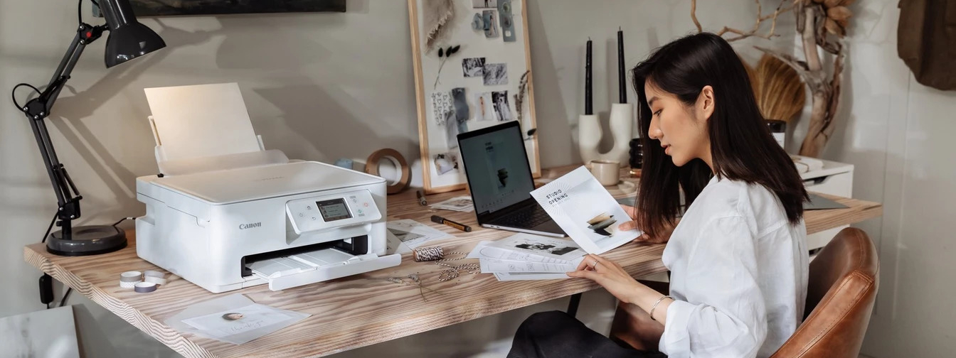 werkende vrouw zittend aan een bureau met een laptop, Canon printer en decoraties